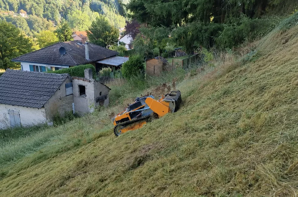 Ferngesteuerte Mähraupe bei der Pflege einer steilen Hangfläche oberhalb eines Wohngebiets.